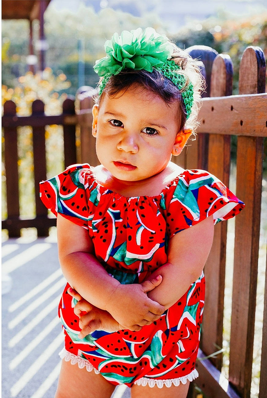Lya participe au concours pour gagner de l'argent avec cette photo : baby_toddler_clothing, child, clothing, dress, face, fence, fun, green, happy, human_body, leisure, person, pink, plant, shorts, sleeve, standing, summer, thigh, toddler