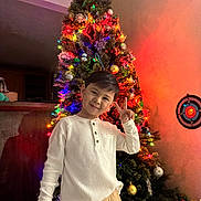 Tyler is registered to the contest to win money with this photo: child, boy, christmas_tree, holiday, festive_lights, ornaments, peace_sign, smile, indoor, celebration, decorations, winter_clothing, happy, portrait, home, seasonal, toy, warm_lighting, casual_clothing, family