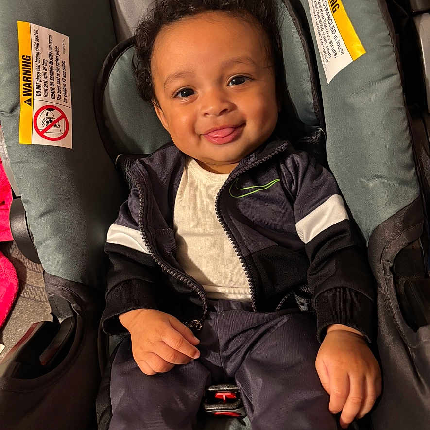 Navir joined the competition — help win amazing prizes! baby, car_seat, child, clothing, curly_hair, cute, face, hands, happy, indoor, infant, jacket, pants, person, playful, portrait, seat, sitting, smiling, young_child