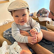 Elio a rejoint le concours — aidez-le/la à gagner de superbes lots ! adult, arm, baby, background, cap, child, clothing, cozy, cute, face, foot, hand, happy, holding, indoor, infant, person, playful, portrait, smile