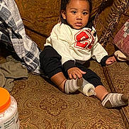 Givenchy joined the competition — help win amazing prizes! baby, blanket, bottle, child, clothing, comfort, couch, cozy, curly_hair, expression, face, furniture, hand, indoor, patterned_fabric, portrait, sitting, socks, toddler, young_child