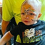 Ranger is registered to the contest to win money with this photo: toddler, child, face_paint, portrait, black_shirt, text_on_shirt, person, indoor, sitting, cute, blond_hair, blue_eyes, tattooed_arm, yellow_shirt, parent, closeup, expression, costume, halloween, casual