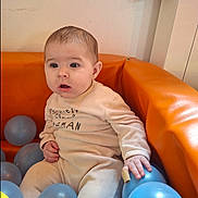Noa a rejoint le concours — aidez-le/la à gagner de superbes lots ! baby, infant, child, sitting, orange_sofa, ball_pit, blue_ball, balls, onesie, clothing, hand, face, eyes, surprised_expression, indoor, wall, play_area, portrait, cute, soft_furniture