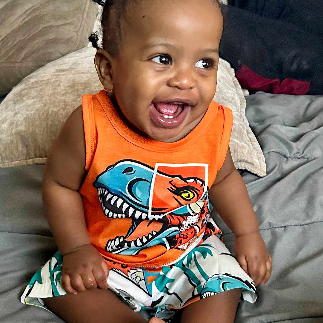 Malachi joined the competition — help win amazing prizes! toddler, child, smiling, dinosaur_print, orange_tank_top, shorts, bed, pigtails, happy, indoors, cute, person, clothing, sitting, feet, portrait, baby, furniture, cushion, skin
