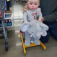 Amelia joined the competition — help win amazing prizes! adult_hand, baby, child, clothing, cute, floor, gold_shoe, grandparent, infant, plush_elephant, portrait, pout_expression, rocking_toy, rosy_cheeks, shelves, shopping, sneaker, store_aisle, tile_floor, toy