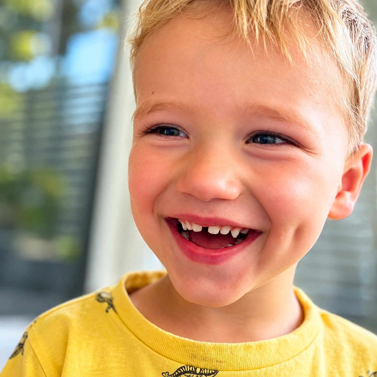Simon joined the competition — help win amazing prizes! child, smiling, portrait, close_up, blond_hair, blue_eyes, tooth_gap, teeth, happy, face, head, yellow_shirt, toddler, young_person, indoor, sunlight, window, blurred_background, photography, joy
