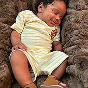 Jahmir is registered to the contest to win money with this photo: baby, sleeping, infant, yellow_striped_clothing, winnie_the_pooh_patch, brown_sandals, curly_hair, soft_blanket, cozy, smiling, cute, portrait, child, resting, indoor, furniture, closeup, peaceful, toddler, skin