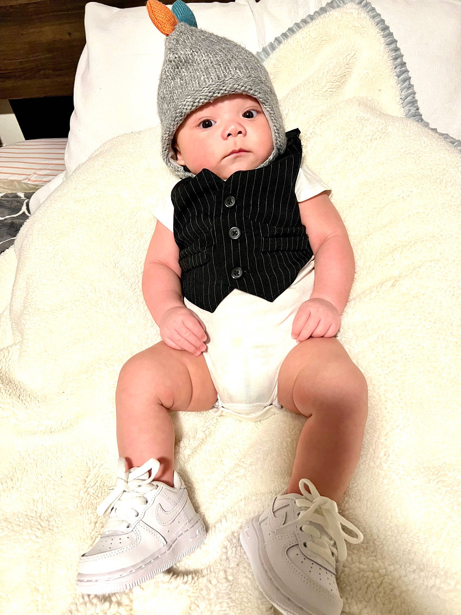 Ezekiel is registered to the contest to win money with this photo: baby, baby_toddler_clothing, cap, child, comfort, costume_hat, embellishment, face, fashion_accessory, fashion_design, headgear, headwear, human_leg, pattern, person, sitting, skin, sleeve, sock, thigh