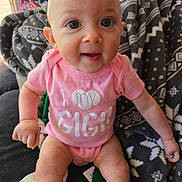 Delilah is registered to the contest to win money with this photo: baby, infant, pink_onesie, sitting, blanket, patterned_blanket, cute, face, big_eyes, child, indoors, clothing, smiling, person, skin, head, arm, leg, happy, young_child