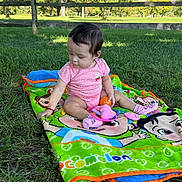 Isabella joined the competition — help win amazing prizes! baby, blanket, cartoon_blanket, child, dark_hair, face, fence, grass, nature, orange_toy, outdoor, park, pink_clothing, polka_dots, portrait, sitting, sunlight, toddler, toy, trees