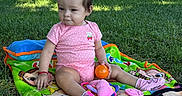 Isabella is registered to the contest to win money with this photo: baby, blanket, cartoon_blanket, child, fence, grass, nature, orange_ball, outdoor, park, pink_clothing, playtime, polka_dots, portrait, sitting, smiling, socks, sunlight, toy, trees