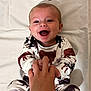 baby, infant, smiling, happy, hand, holding, clothing, animal_print, lying_down, white_background, person, child, cute, joyful, face, skin, eyes, mouth, expression, indoor