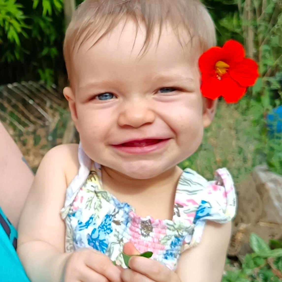 Norah participe au concours pour gagner de l'argent avec cette photo : baby, child, cute, dress, flower, greenery, happy, headwear, holding, leaf, nature, outdoor, person, plant, portrait, red_flower, smiling, summer, sunlight, toddler