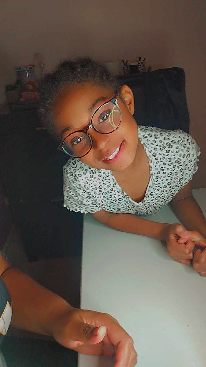 Jalina participe au concours pour gagner de l'argent avec cette photo : child, glasses, smile, table, hand, indoor, person, leisure, portrait, young, casual, clothing, face, happy, human, furniture, skin, arm, eyewear, friendly