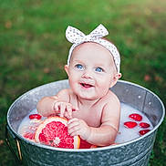 Emerson is registered to the contest to win money with this photo: baby, infant, bucket, milk_bath, grapefruit, strawberries, headband, outdoor, grass, happy, smiling, blue_eyes, skin, fruit, water, playful, summer, cute, child, nature