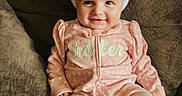 Cassandra Mosier joined the competition — help win amazing prizes! baby, child, pink_onesie, bunny_ears, couch, brown_couch, smiling, cute, indoor, portrait, infant, comfortable, seated, playful, adorable, headwear, face, small_child, happy, young