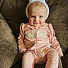 baby, child, pink_onesie, bunny_ears, couch, brown_couch, smiling, cute, indoor, portrait, infant, comfortable, seated, playful, adorable, headwear, face, small_child, happy, young