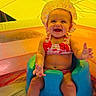 baby, child, smiling, swimsuit, bonnet, blue_seat, pool, water, umbrella, yellow, summer, outdoor, happy, sitting, playful, cute, infant, legs, feet, sunlight