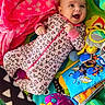 Cassandra Mosier is registered to the contest to win money with this photo: baby, infant, playpen, toy, blanket, smile, onesie, colorful, happy, child, face, play, fabric, pattern, cute, lying_down, indoors, soft_toy, baby_toy, comfort