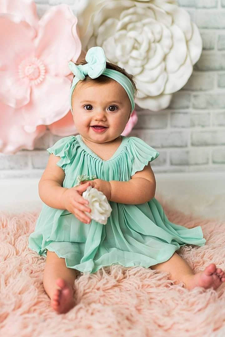 Miley is registered to the contest to win money with this photo: aqua, baby, baby_toddler_clothing, cheek, child, clothing, dress, happy, headgear, headpiece, iris, joy, person, petal, picture_frame, pink, product, sitting, sleeve, smile