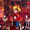 toddler, child, mickey_mouse, red_sweater, jeans, barefoot, chair, teddy_bear, toy_soldier_costume, fireplace, holiday_decorations, christmas_lights, red_carpet, festive, indoors, holiday_scene, decor, smiling, portrait, warm_lighting