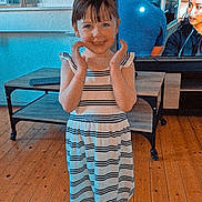 Chelsea participe au concours pour gagner de l'argent avec cette photo : child, girl, striped_dress, barefoot, wooden_floor, living_room, table, television, smiling, happy, indoor, furniture, person, flooring, casual_clothing, home, standing, hands, young, playful