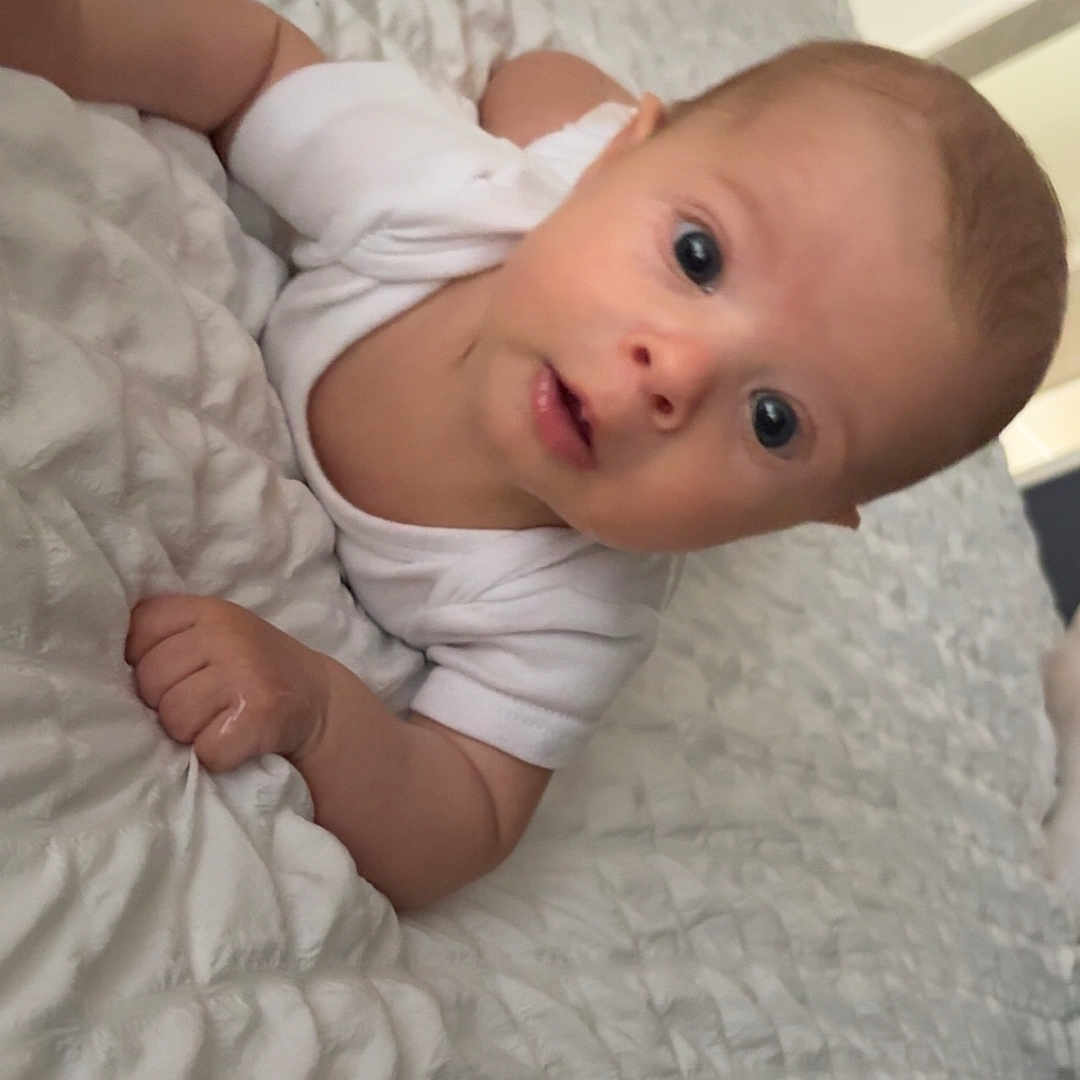 Eden a rejoint le concours — aidez-le/la à gagner de superbes lots ! arm, baby, bed, blanket, candid, child, curious, expression, eyes, face, hand, head, indoors, infant, lying_down, portrait, skin, soft_lighting, texture, white_clothing