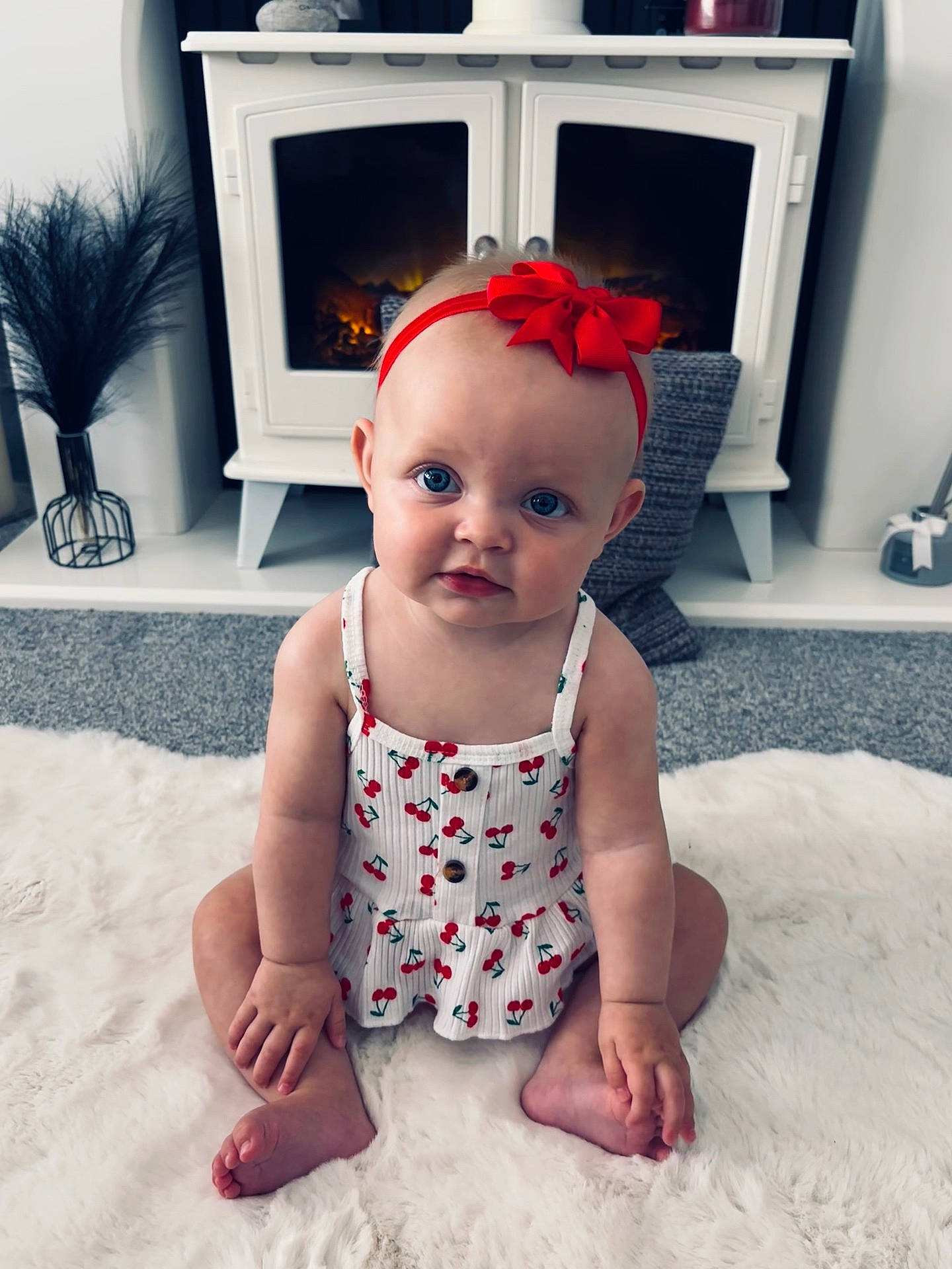Marnie joined the competition — help win amazing prizes! baby, blue_eyes, carpet, cherry_pattern, child, cozy, curious, cute, dress, feet, fireplace, fluffy_rug, hands, headband, indoor, infant, portrait, red_bow, sitting, smiling