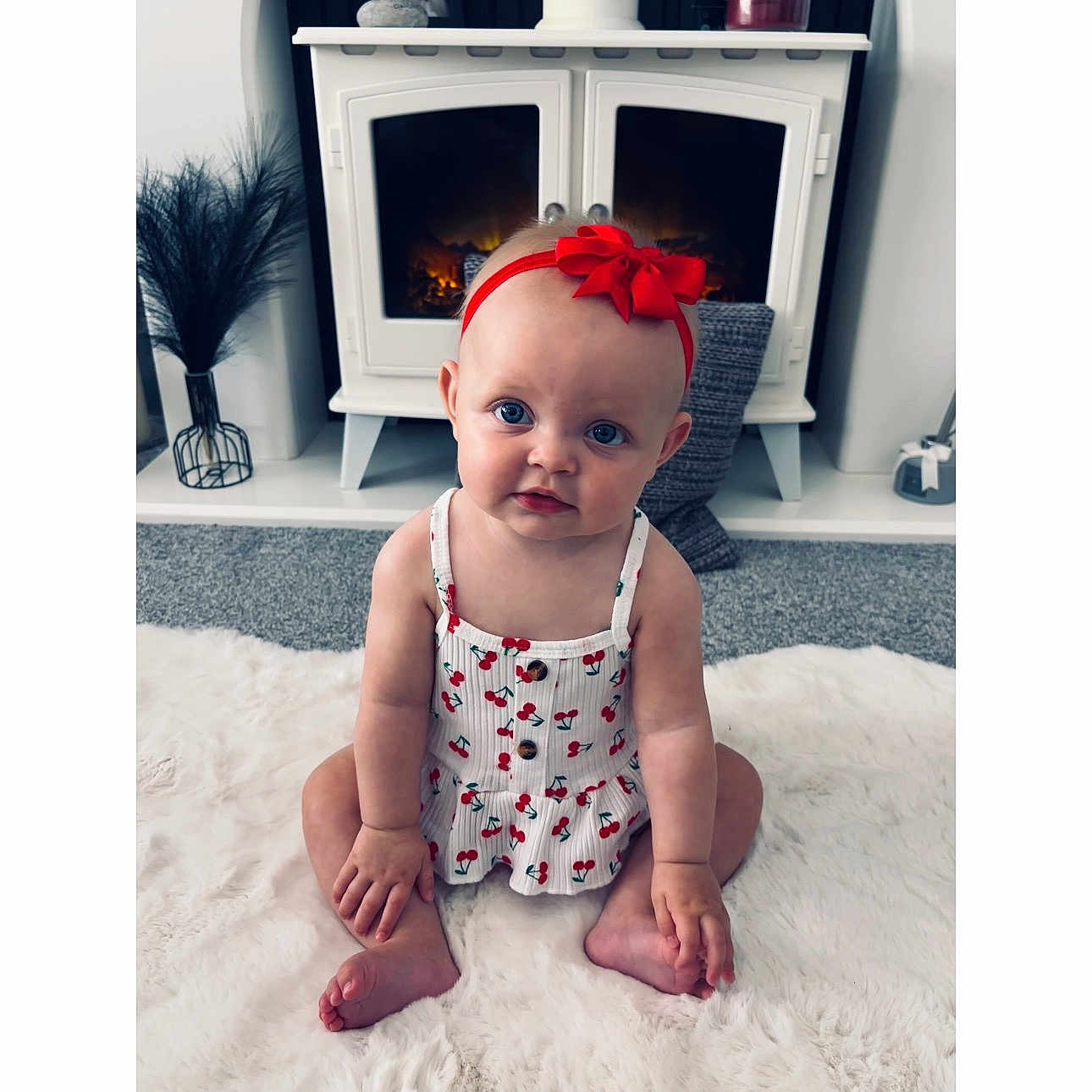 Marnie joined the competition — help win amazing prizes! baby, child, headband, red_bow, blue_eyes, cherry_pattern, dress, sitting, white_rug, fireplace, cozy, indoor, carpet, curious, portrait, cute, homedecor, floor, infant, hands
