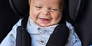 Teddy is registered to the contest to win money with this photo: baby, car_seat, child, infant, smiling, happy, pacifier, safety_harness, onesie, cute, seatbelt, black, white_clothing, indoor, closeup, small_child, infant_face, baby_clothes, hands, head
