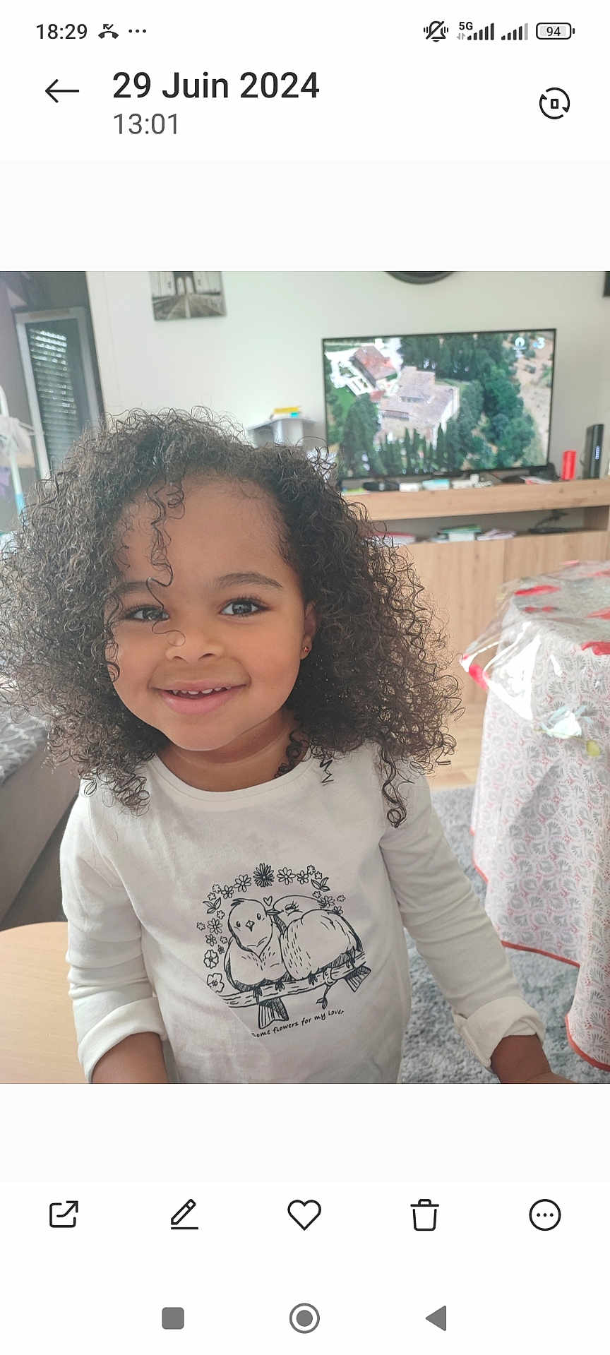 Kélya participe au concours pour gagner de l'argent avec cette photo : child, curly_hair, smiling, white_shirt, bird_illustration, living_room, television, table, tablecloth, sofa, carpet, earrings, indoor, person, furniture, home, portrait, happy, cute, young_child