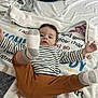baby, child, sock, striped_shirt, brown_pants, blanket, lying_down, foot, raised_leg, indoor, soft_texture, curious_expression, person, clothing, face, head, infant, cute, playful, resting