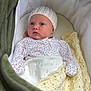 baby, infant, knit_hat, floral_onesie, blanket, crocheted_blanket, bassinet, cozy, sleepwear, newborn, child, cute, face, portrait, indoors, soft_lighting, resting, comfortable, warm, sleep