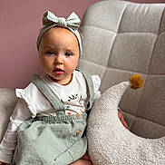 Mència participe au concours pour gagner de l'argent avec cette photo : toddler, child, headband, dress, pillow, crescent_moon, pom_pom, chair, cushion, pink_wall, indoor, sitting, curious, portrait, baby, clothing, soft_texture, person, cute, furniture