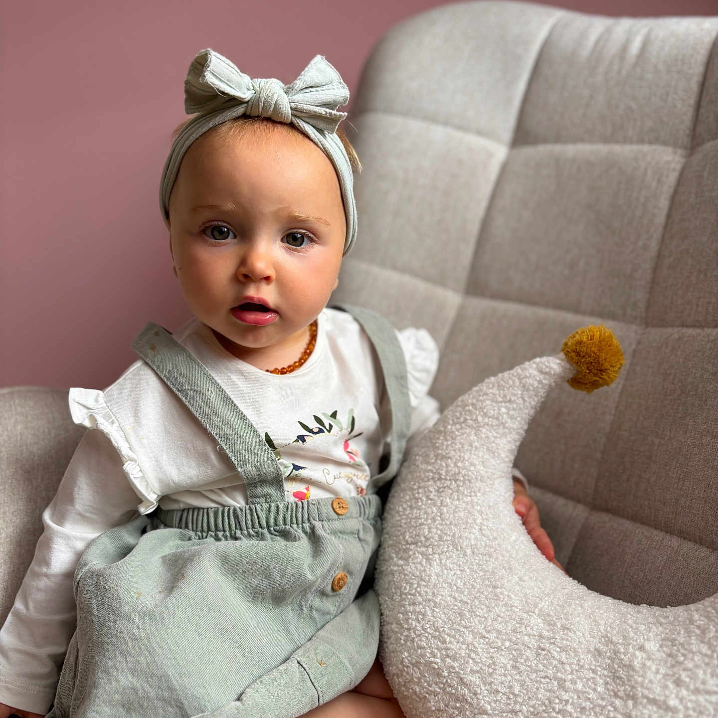 Mència participe au concours pour gagner de l'argent avec cette photo : baby, chair, child, clothing, crescent_moon, curious, cushion, cute, dress, furniture, headband, indoor, person, pillow, pink_wall, pom_pom, portrait, sitting, soft_texture, toddler