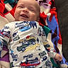 baby, smiling, onesie, blanket, colorful, infant, child, clothing, patterned, happy, cute, lying_down, face, fun, playful, indoor, person, toddler, fabric, cozy