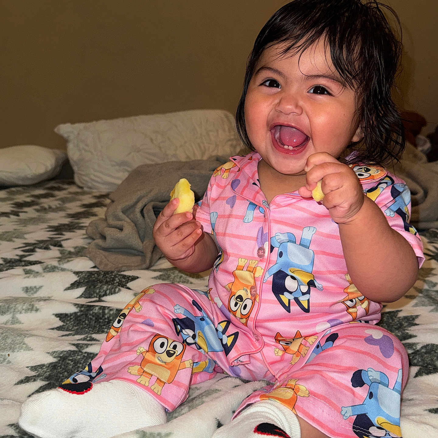 Madison is registered to the contest to win money with this photo: toddler, child, pajamas, smiling, laughing, bed, blanket, socks, indoor, cute, happy, snack, person, face, hair, clothing, pattern, furniture, home, cozy