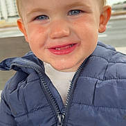Maël participe au concours pour gagner de l'argent avec cette photo : child, toddler, face, blue_eyes, smile, jacket, zipper, drool, blond_hair, short_hair, cheek, ear, nose, teeth, outdoor, portrait, closeup, happy, bench, building