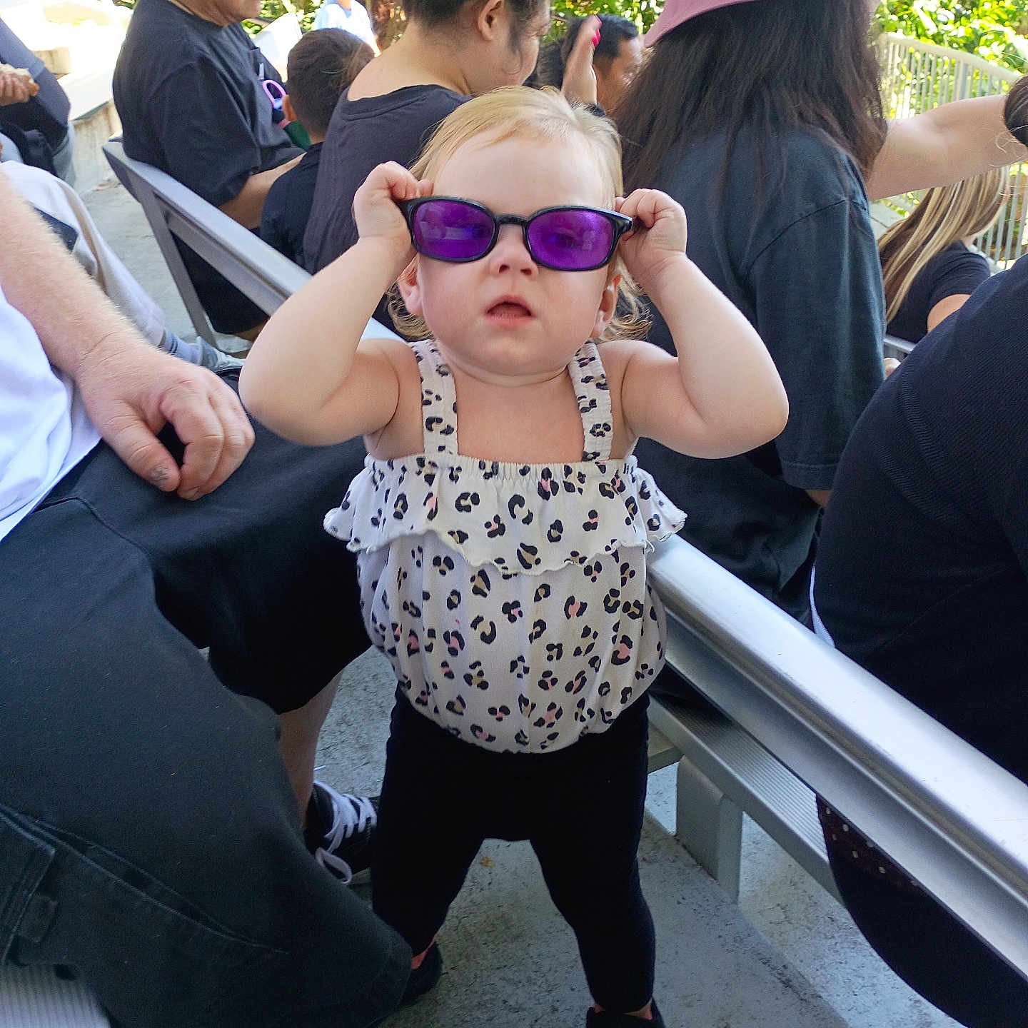 Winter joined the competition — help win amazing prizes! child, toddler, sunglasses, purple_glasses, standing, outdoor, sunlight, crowd, adults, seated_people, portrait, fashion, dress, leopard_print, hair_bow, playful, funny, railings, chairs, park