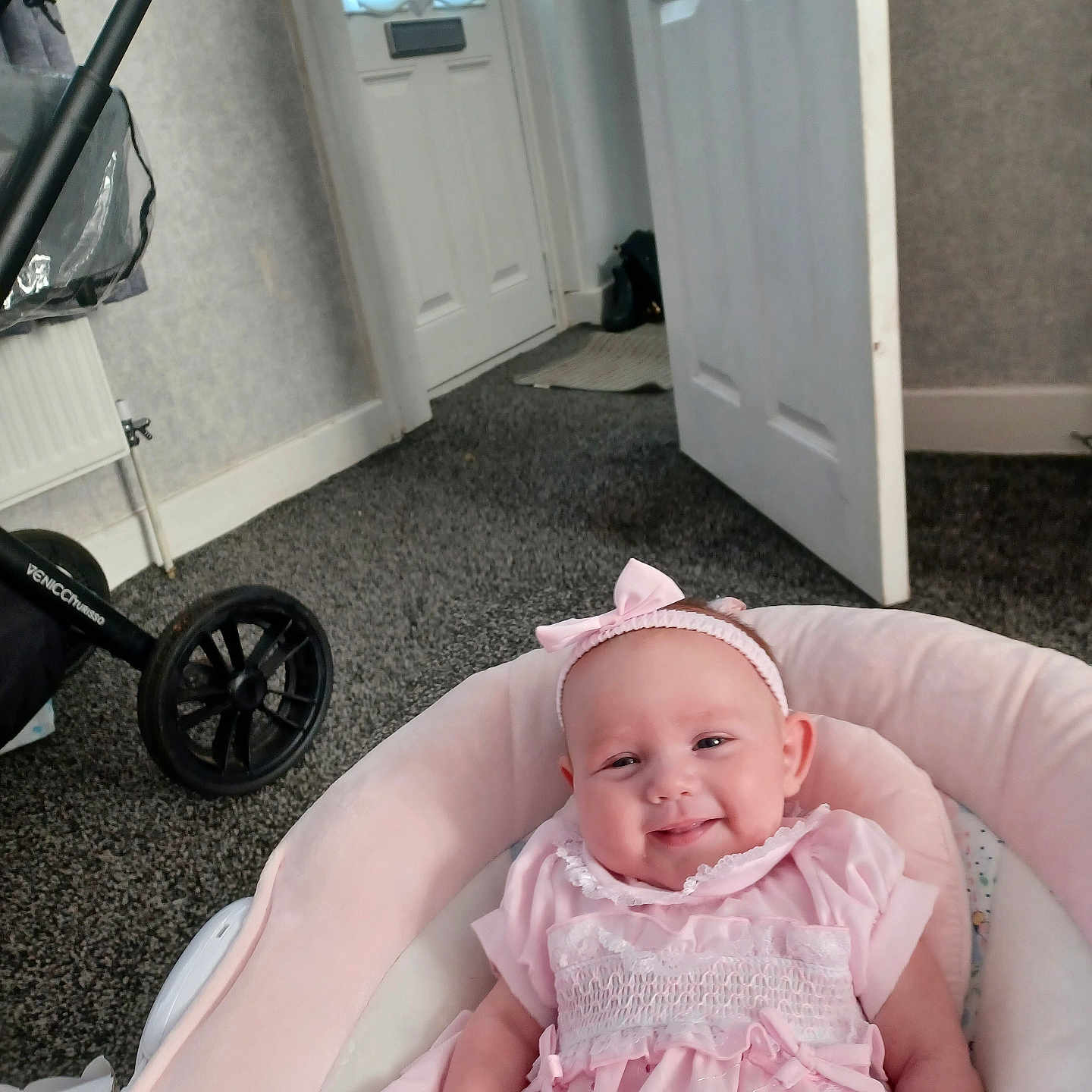Ava is registered to the contest to win money with this photo: baby, baby_seat, carpet, child, clothing, cushion, door, floor, happy, headband, home_interior, indoor, infant, person, pink_dress, portrait, seated, smile, stroller, young_child