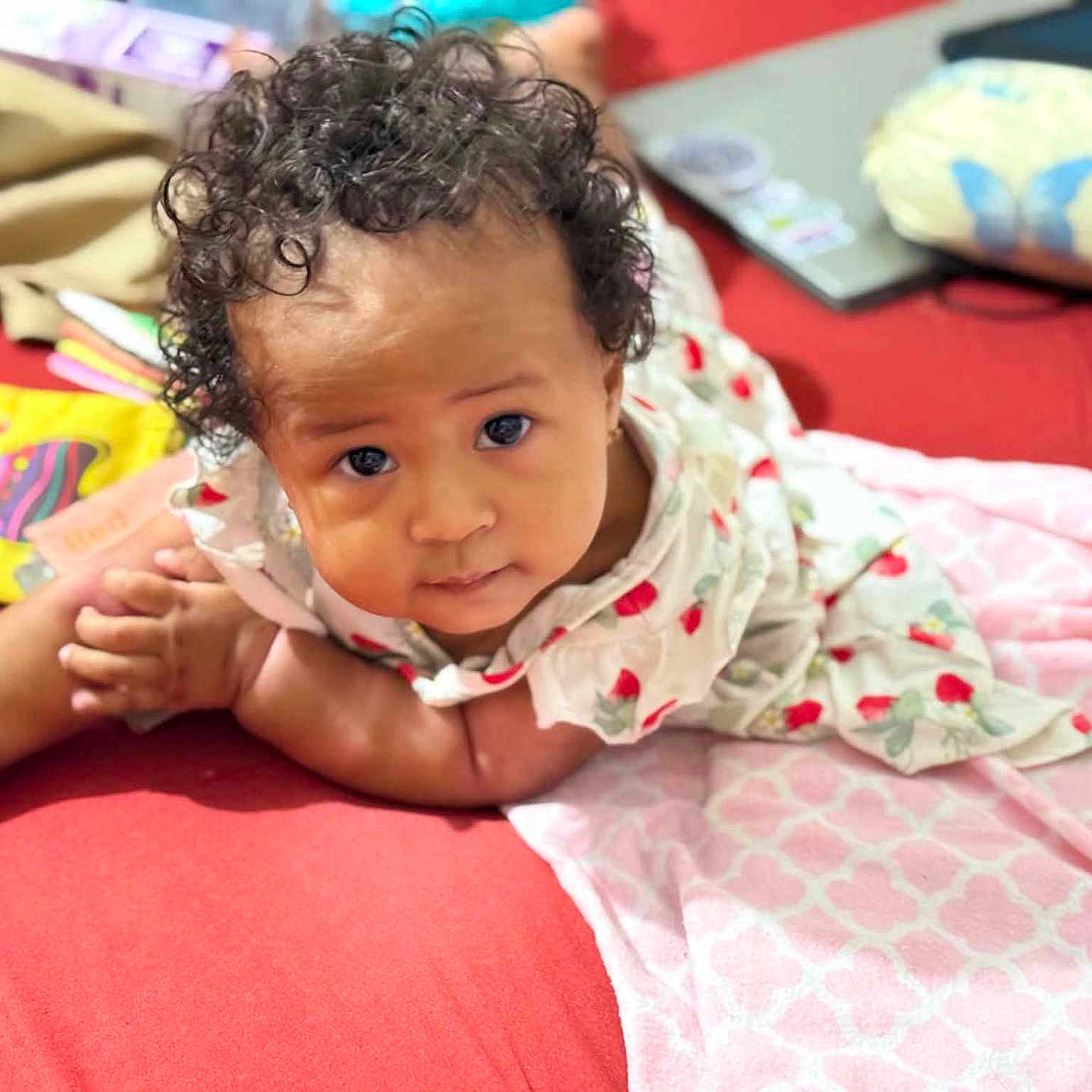 Lanayah-La'Raa joined the competition — help win amazing prizes! baby, curly_hair, red_surface, dress, strawberry_pattern, blanket, laptop, indoor, child, cute, gaze, expression, infant, lying_down, homely, soft_lighting, portrait, closeup, comfortable, cozy