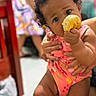 Lanayah-La'Raa is registered to the contest to win money with this photo: baby, child, curly_hair, bread, pink_outfit, hands, indoor, person, cute, food, holding, close_up, expression, skin, legs, background, blur, dress, support, people