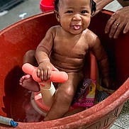 Lanayah-La'Raa is registered to the contest to win money with this photo: baby, child, bathtub, red_tub, toy, water, playful, smiling, tongue_out, hands, adult, indoor, floor, wet_skin, cute, happy, sitting, person, bath_time, fun