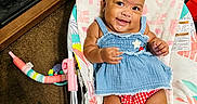 A Marie joined the competition — help win amazing prizes! baby, child, smiling, blue_dress, red_shorts, baby_rocker, indoor, carpet, toys, fireplace, cute, happy, infant, person, seat, playroom, colorful, smile, comfort, home