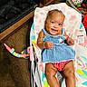 baby, child, smiling, blue_dress, red_shorts, baby_rocker, indoor, carpet, toys, fireplace, cute, happy, infant, person, seat, playroom, colorful, smile, comfort, home