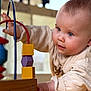 baby, infant, child, toy, wooden_toy, bead_maze, close_up, portrait, blue_eyes, hand, sleeve, clothing, play, indoor, wooden_blocks, curiosity, face, expression, soft_lighting, playing