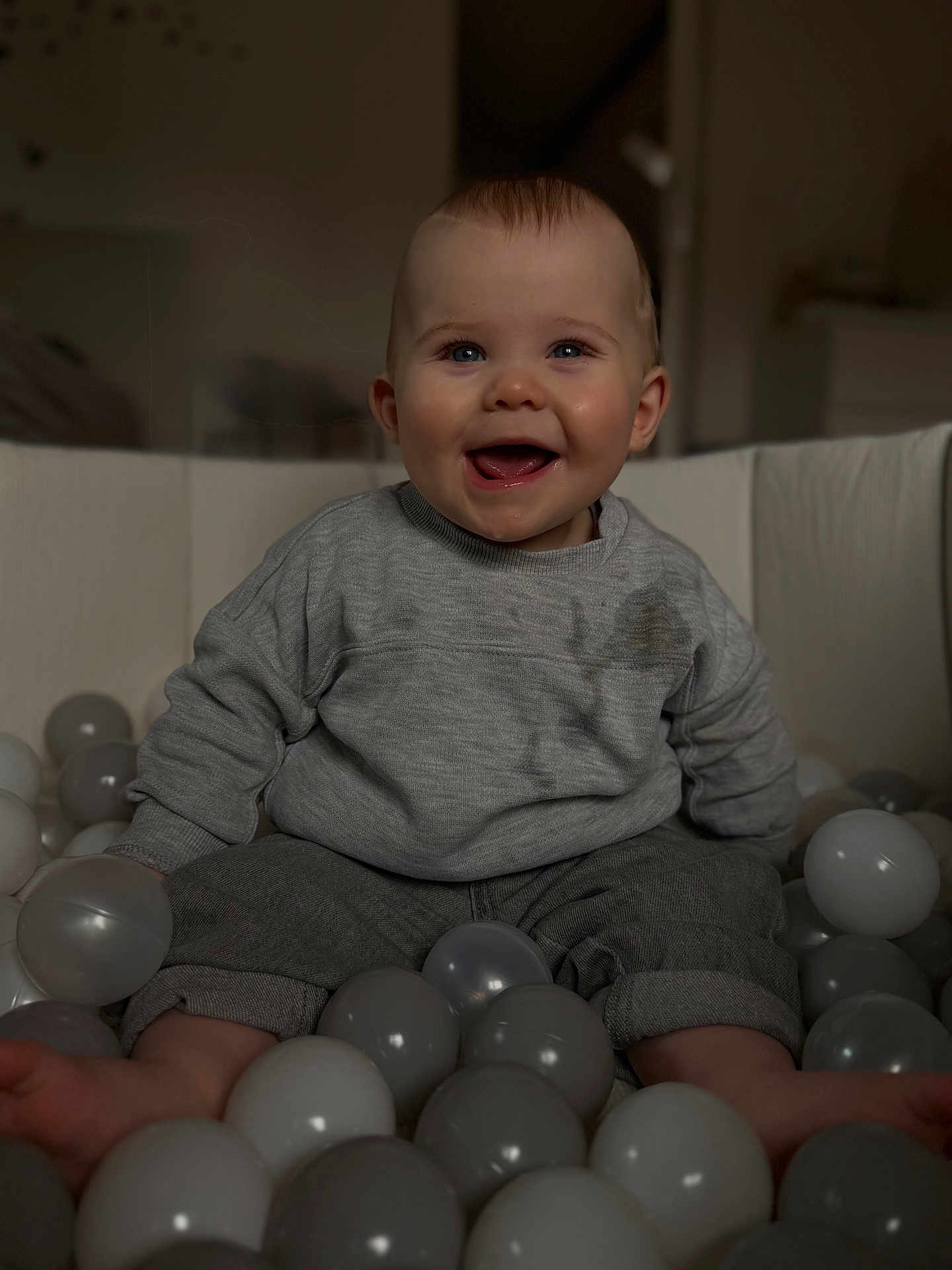 Eden participe au concours pour gagner de l'argent avec cette photo : baby, infant, smiling, laughing, ball_pit, plastic_balls, grey_balls, sweater, stained_clothing, sitting, indoor, portrait, cute, cheeks, blue_eyes, mouth_open, teeth, short_hair, soft_lighting, playful