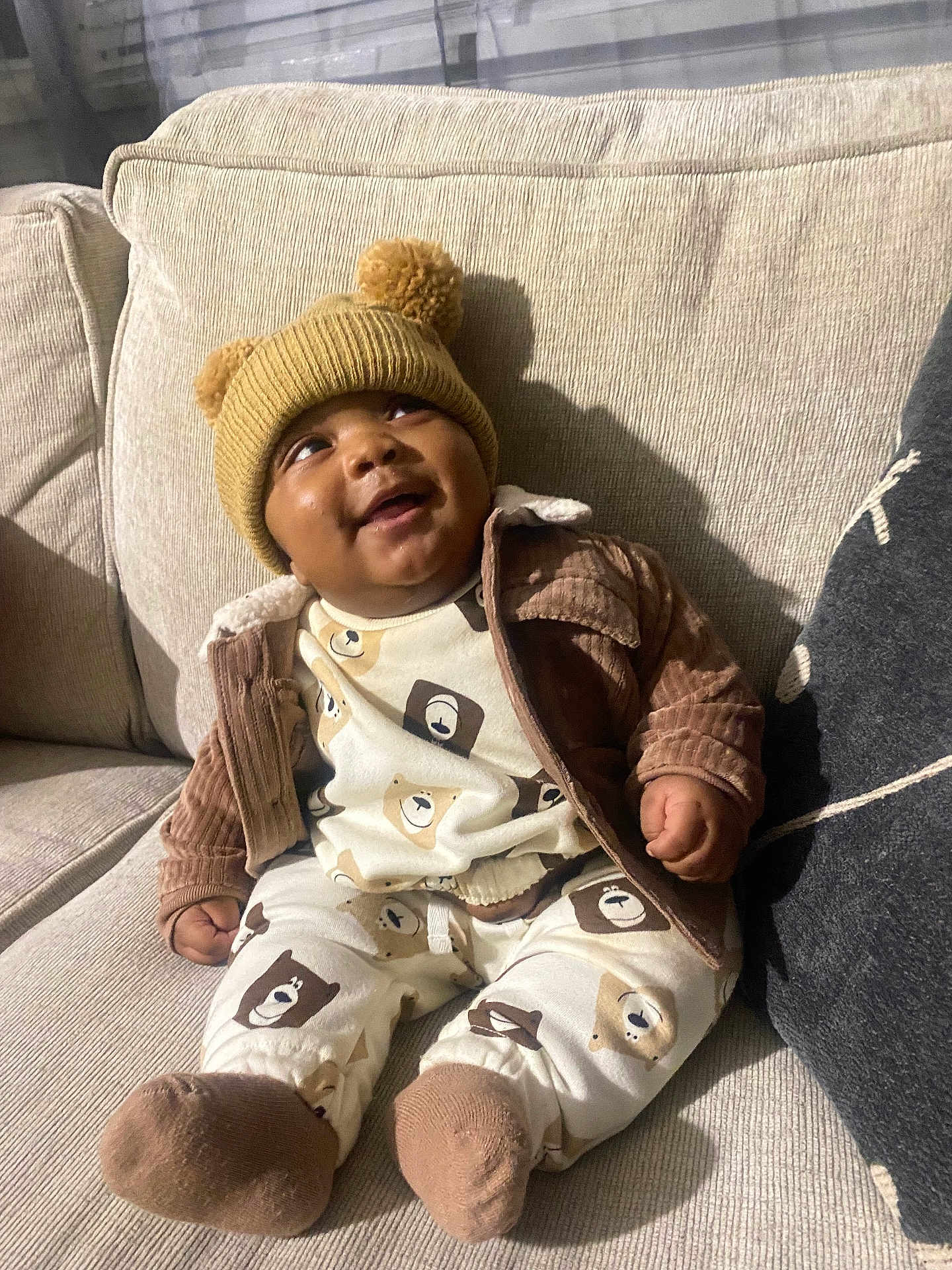 Jett joined the competition — help win amazing prizes! baby, child, smiling, pajamas, hat, pom_poms, couch, beige, brown, cream, bear_pattern, clothing, indoor, cozy, happy, person, sitting, cute, infant, portrait