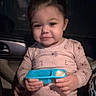 toddler, child, car, snack, container, pink_clothing, maroon_pants, seat, interior, seatbelt, person, face, smile, hand, holding, cute, indoors, night, window, fabric