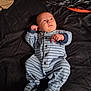 baby, infant, onesie, striped_clothing, bed, blanket, sleepwear, child, person, cute, small_hands, face, looking_up, lying_down, indoors, soft_fabric, cozy, newborn, pajamas, resting